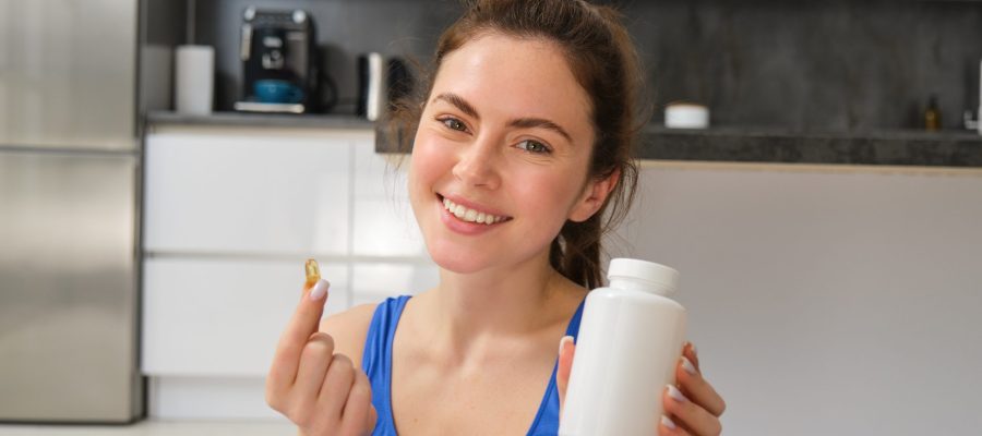 Happy young fit girl, doing sports at home, shows dietary supplements, taking vitamins for healthy body, recommending, showing drug capsule.