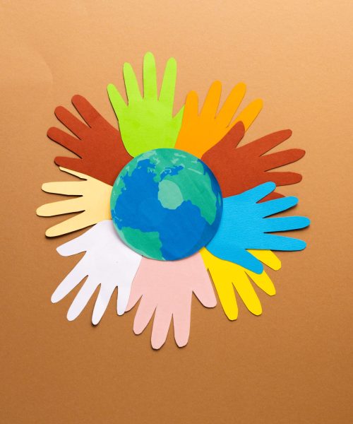 Paper cut out of multi coloured hands and globe with copy space on brown background. Humanitarian aid, people, help and human concept.