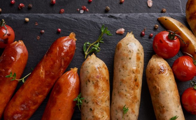 sausages and ingredients for cooking. Grilled sausage with the addition of herbs and and spices, vegetables, rosemary, thyme on the grill plate, Grilling food, bbq, barbecue, on stone table. Top view.